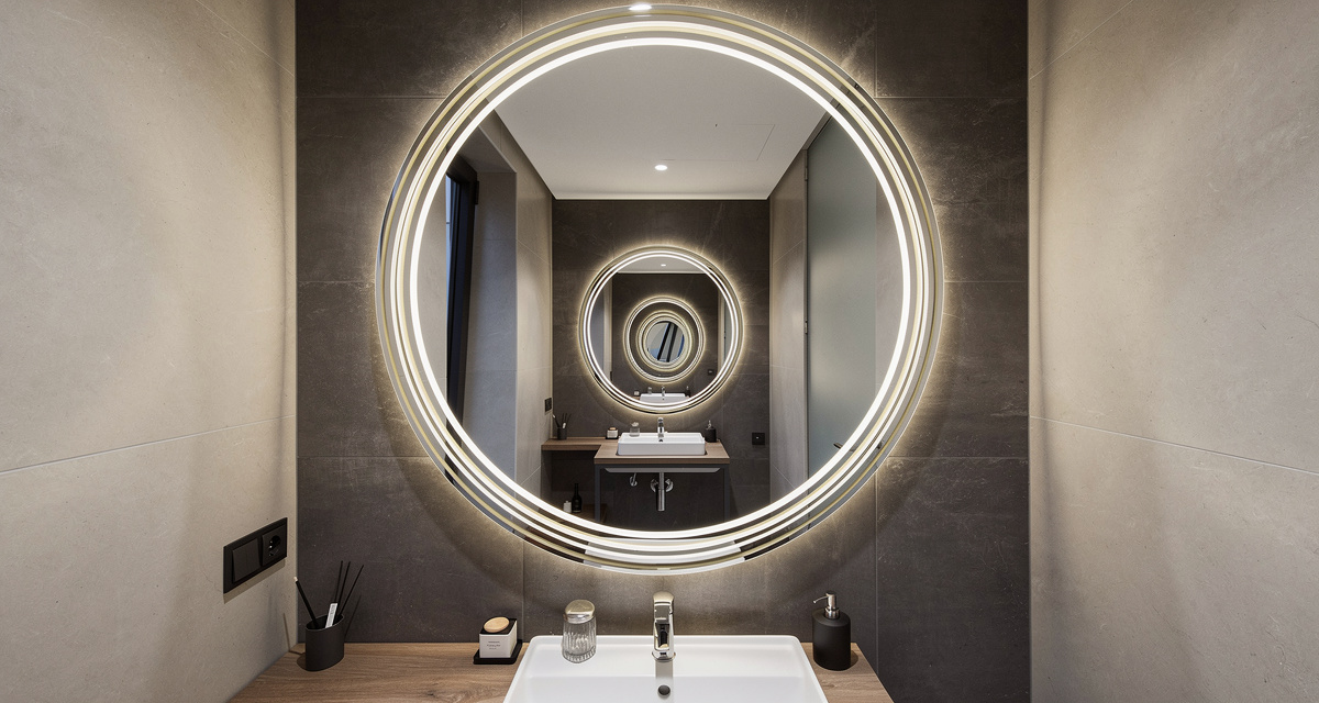 An oversized Guocio Art Mirror reflecting light and visually doubling the size of a small bathroom.
