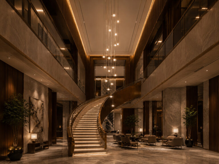 Five-star hotel atrium staircase with Guocio cascading multi-tier pendant chandeliers spanning two floors creating waterfall lighting effect